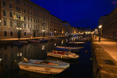 Boats moored on canal by illuminated buildings in city at night