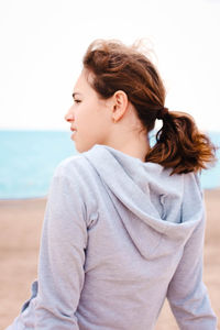 Rear view of girl sitting at beach against clear sky