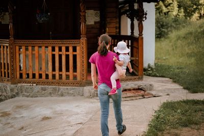 Rear view of mother and girl standing against building