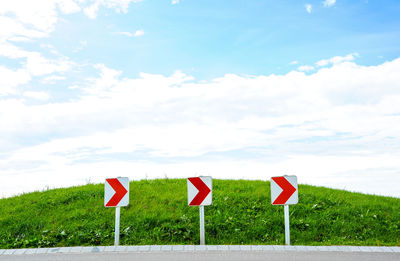 Road sign on field against sky