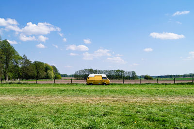 Yellow van on grassy field against blue sky