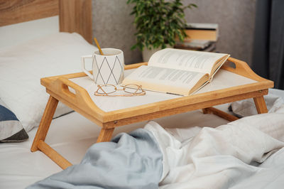 Cup of coffee, book and glasses on bed with soft blanket indoors