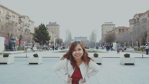 Portrait of young woman standing on city street against clear sky