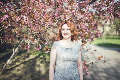 Cheerful middle aged armenian woman in an elegant dress under the blooming sakura tree. spring park 