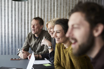 Smiling creative business colleagues sitting at conference table while looking away in board room