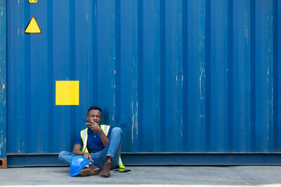 Full length of woman sitting against blue wall