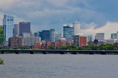 Modern buildings by river against sky in city