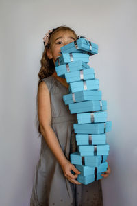 Portrait of young woman holding gift box against wall