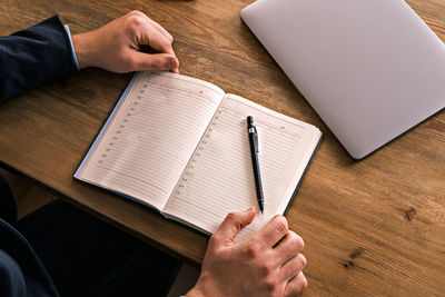 Cropped hands of man writing in book while sitting on table