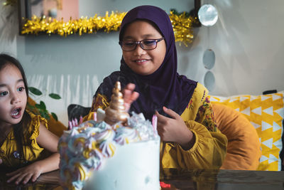 Smiling girl looking at cake while sitting with friend at home