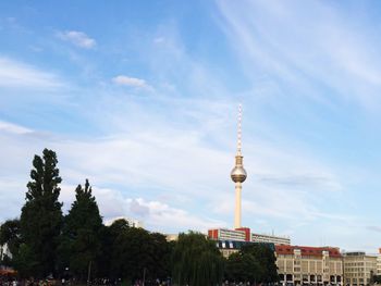 Low angle view of fernsehturm tower by buildings and trees against sky