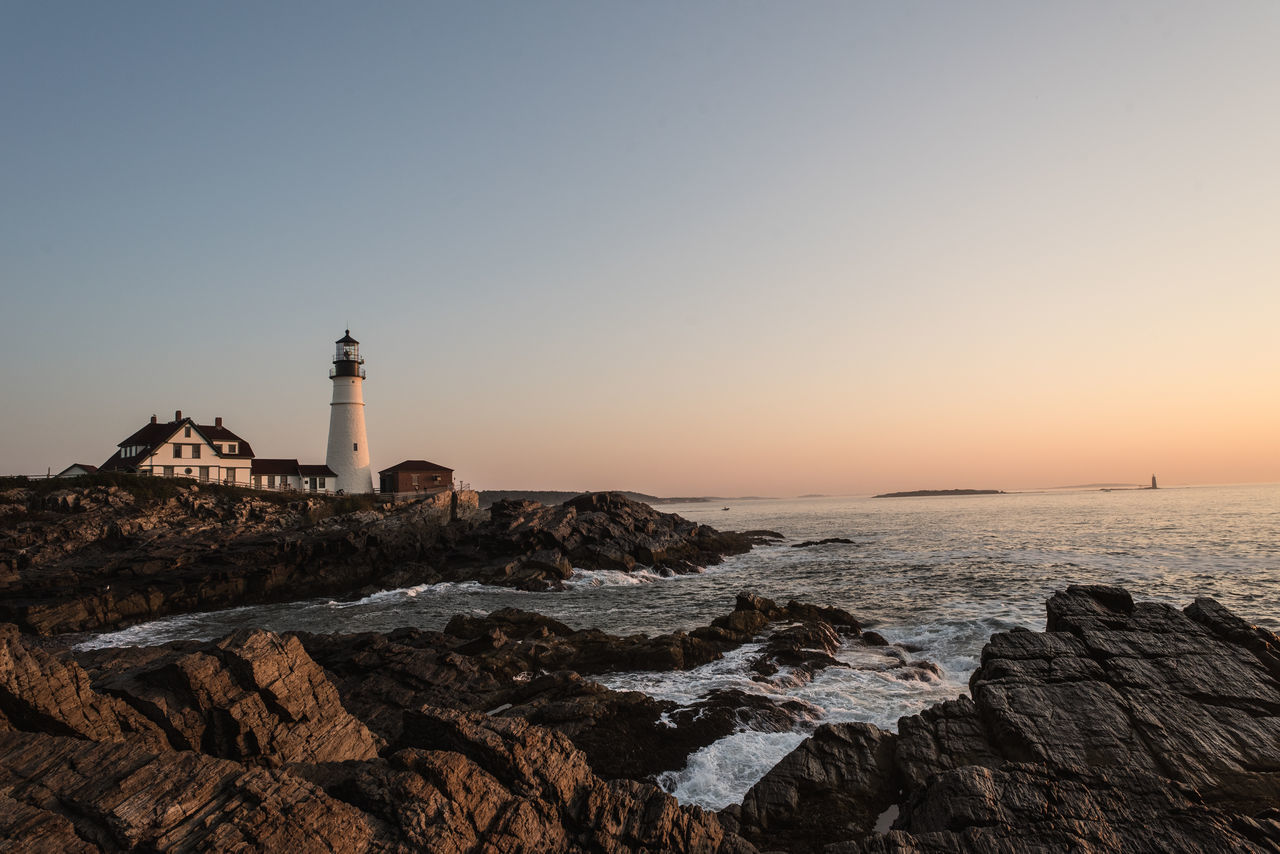 LIGHTHOUSE AMIDST SEA AGAINST CLEAR SKY DURING SUNSET