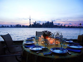 Empty plates arranged on table by river against cityscape