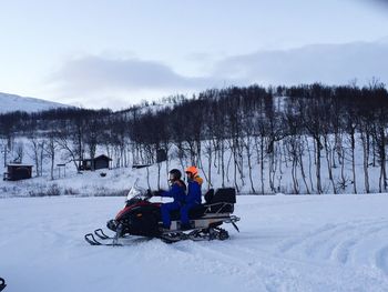 Side view of friends snowmobiling on snowy field against sky