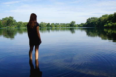 Rear view of woman standing in river against sky