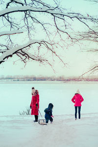 Mother and daughters wearing warm clothing playing in snow during winter