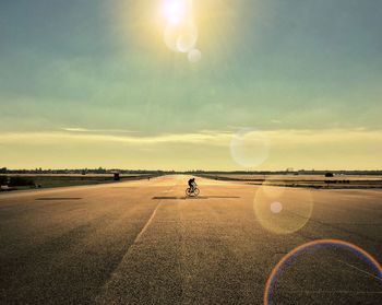 Mid distance view of person riding bicycle on road against sky during sunny day