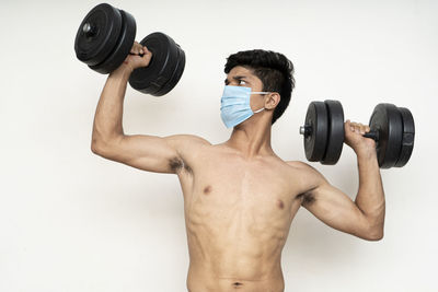 Full length of shirtless man holding camera over white background