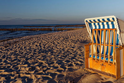 Hooded chairs on beach against clear sky