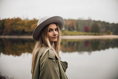 Portrait of woman wearing hat standing by lake