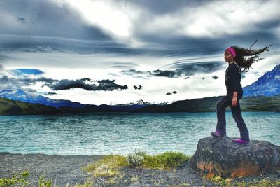 Girl standing on rock by sea against cloudy sky