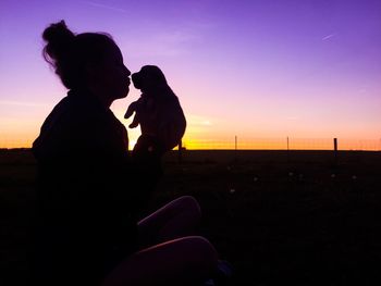 Side view of silhouette woman holding puppy against sky during sunset