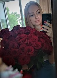 Portrait of woman holding red while standing by window