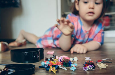 Full length of cute girl playing with toys while lying on hardwood floor at home