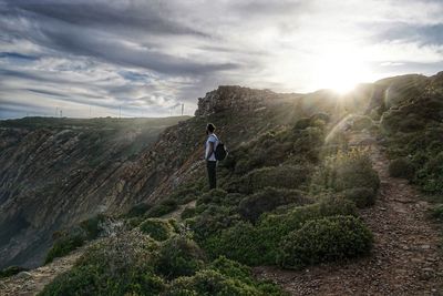 Man standing on mountains against cloudy sky during sunny day