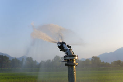 Water spraying on landscape against sky during sunset