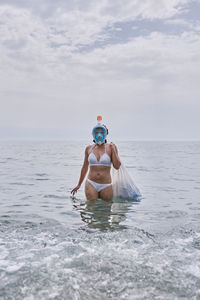 A young girl with diving goggles pulling trash out of the ocean. recycling concept