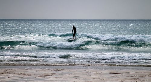 Silhouette surfer surfing in sea against clear sky