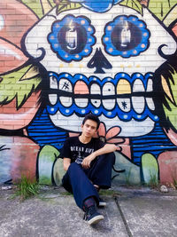 Full length of man sitting against graffiti wall
