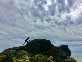 Low angle view of man climbing on rock against sky