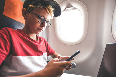 Cute boy using phone while sitting in airplane