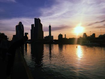 Scenic view of river by buildings against sky during sunset