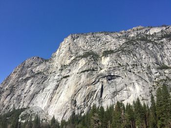 Low angle view of rocky mountain against clear blue sky