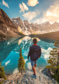 Rear view of man standing on rock over lake against mountains