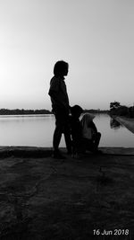 Men sitting on lake against clear sky