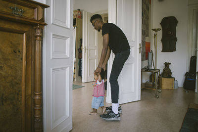 Side view of father assisting daughter in walking at home