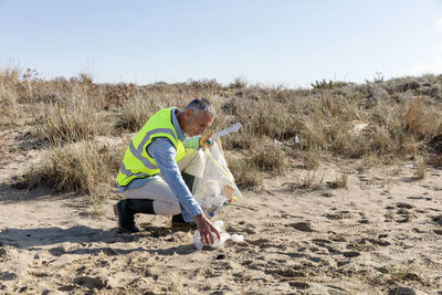 Man collecting garbage kneeling on sand dunes