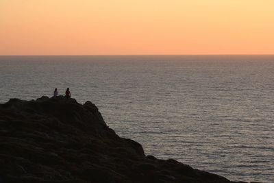 Silhouette people standing on cliff by sea against sky during sunset