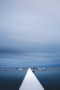 Snow on pier on a moody day against sky