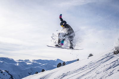 Scenic view of snowboarder jumping mountains against sky