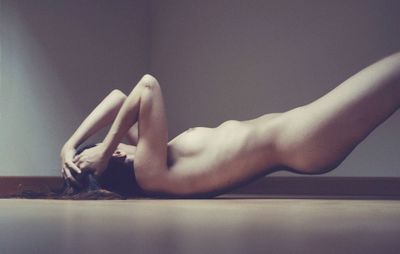 Side view of naked young woman lying on floor at home