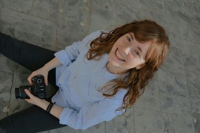 High angle portrait of happy woman sitting on pavement