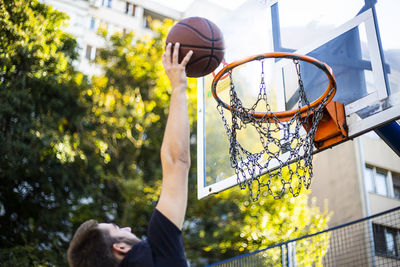 Handsome basketball player shooting a ball through the hoop while playing on basketball court