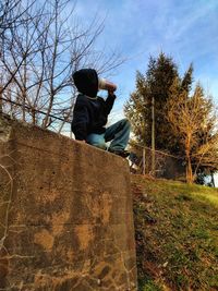 Rear view of man sitting on plant against sky