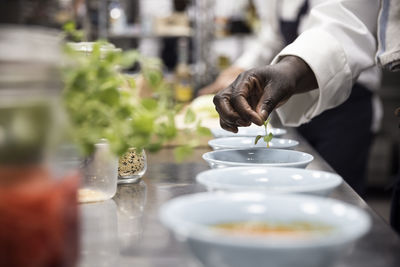 Cropped image of female chef garnishing soup with basil leaf in restaurant