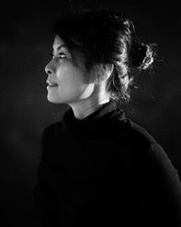 Portrait of young woman looking away against black background